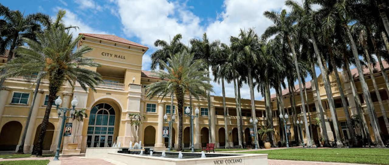 Front view of Miramar City Hall in Florida with palm trees, arches, and fountain.