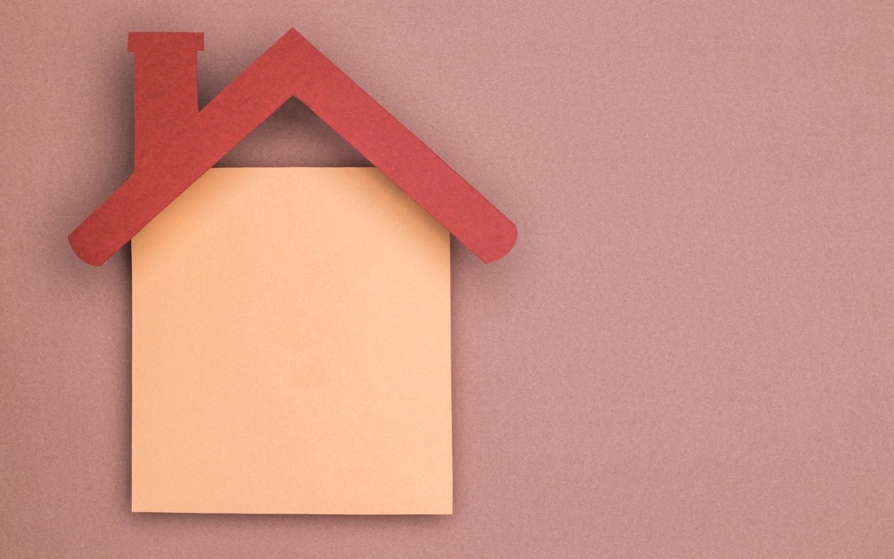 Paper house cutout with a red roof against a muted pink background.