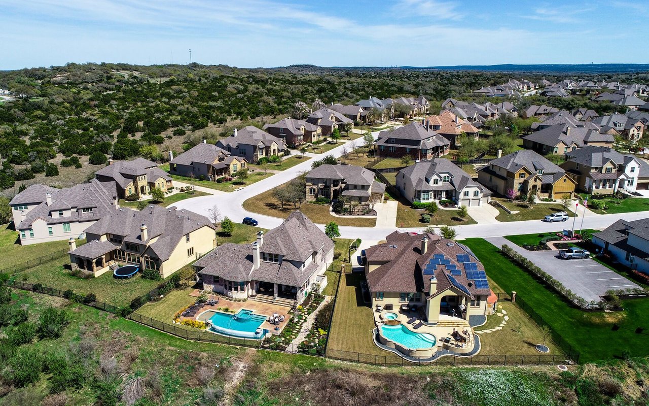 Aerial view of a residential neighborhood with detached homes, backyard pools, and open hills nearby.