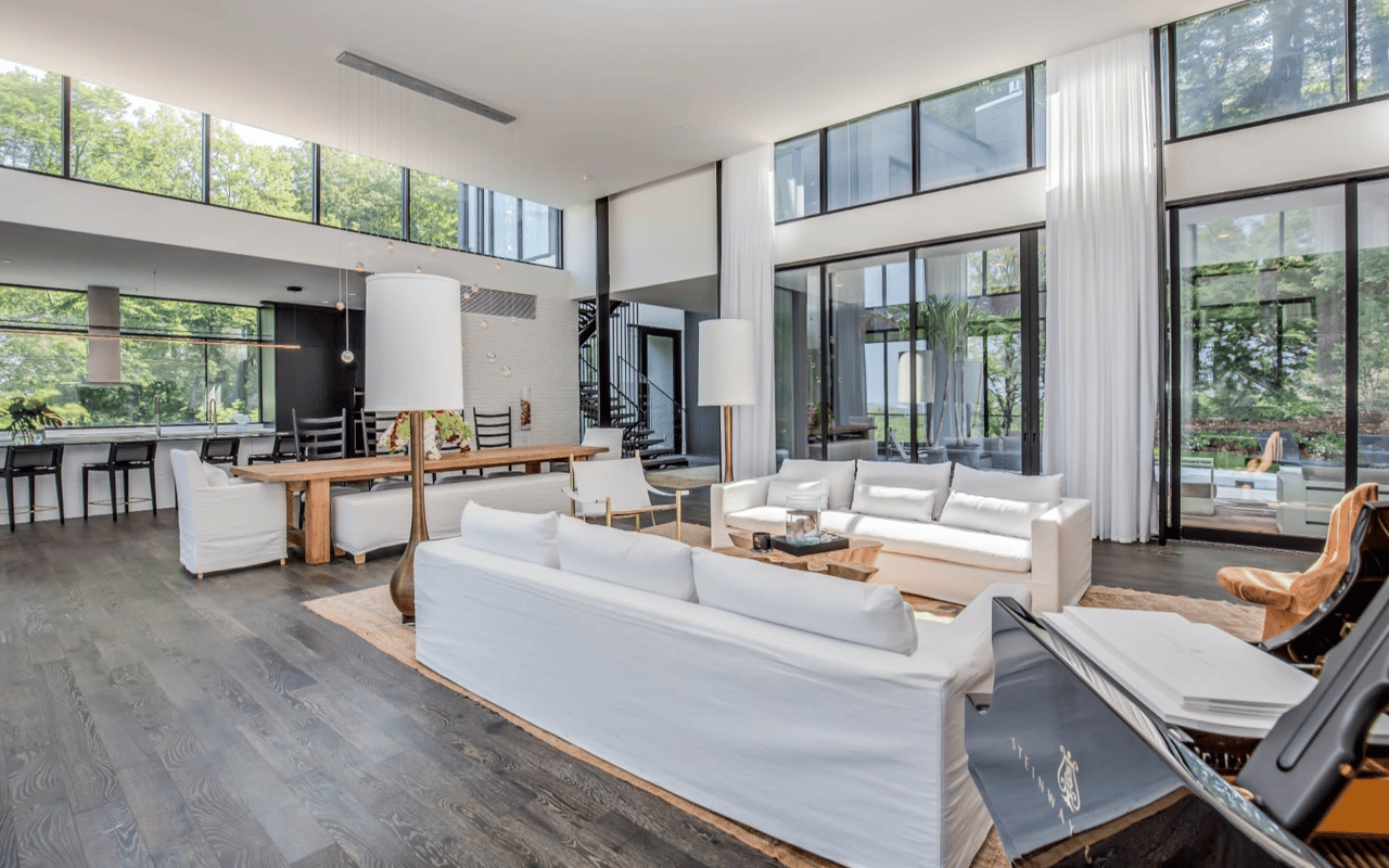 Open-plan living and dining room with white sofas, soaring ceilings, and expansive windows.