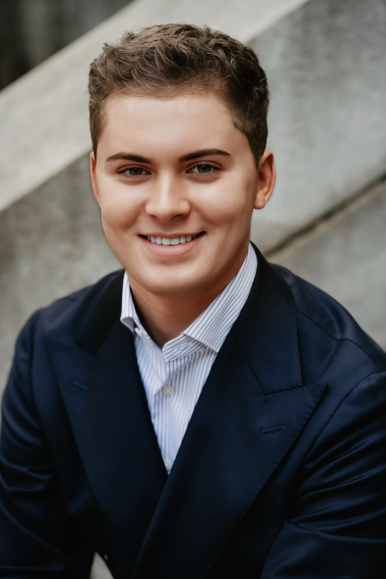 Channing Croft smiling in a dark suit and striped shirt in front of stone steps.
