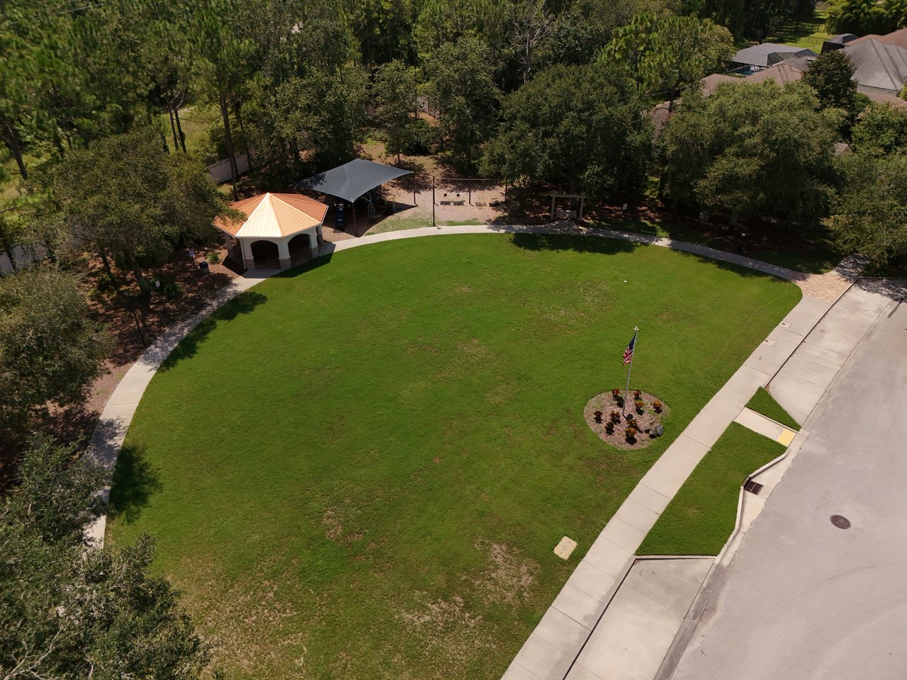Aerial view of a community lawn with curved sidewalks, a pavilion, and a shaded playground.
