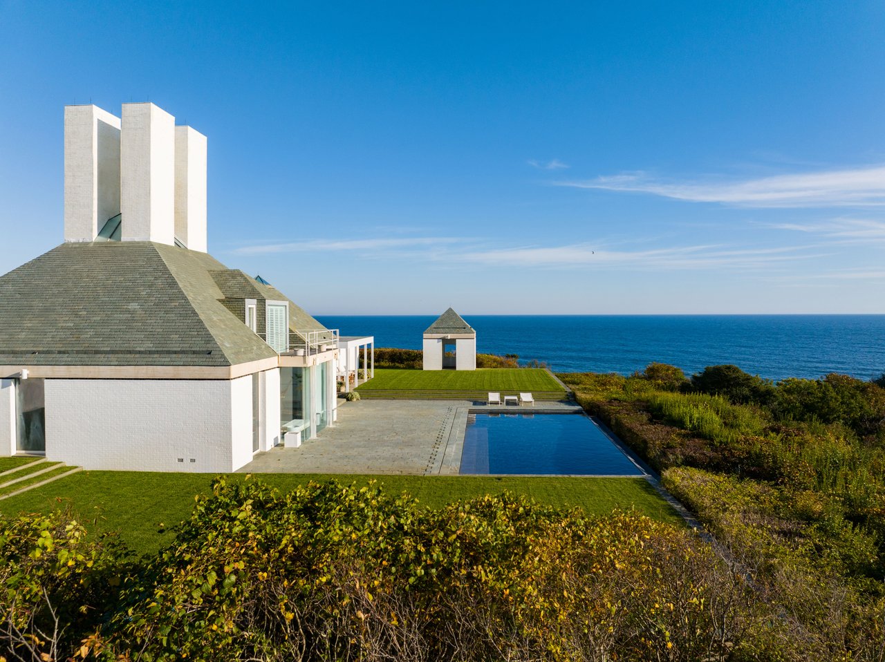 Modern white coastal home with a pool and lawn overlooking the ocean.