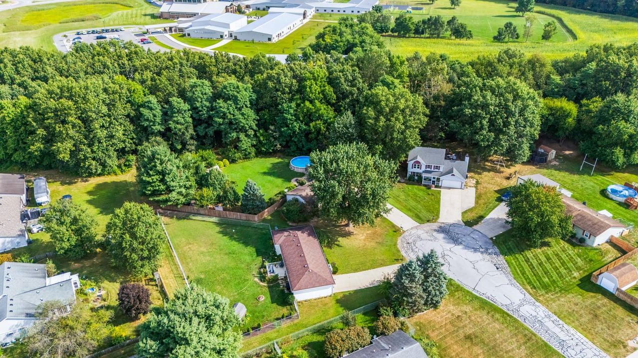 Aerial view of a two-story house with a tree-lined backyard and blue above-ground pool.