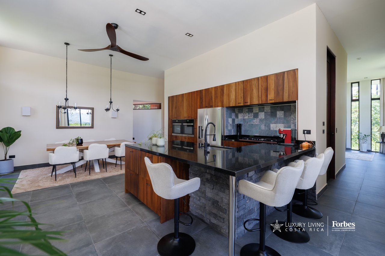 Modern kitchen with wood cabinetry, a black stone island, and an adjoining dining area.