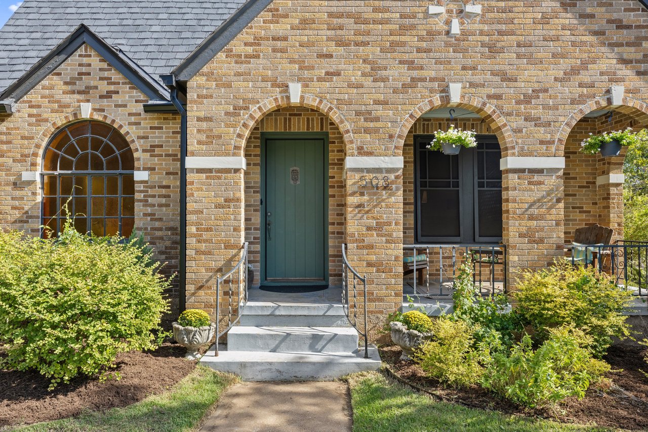 Brick house entrance with arched porch openings, green door, landscaped steps, and the number 508.