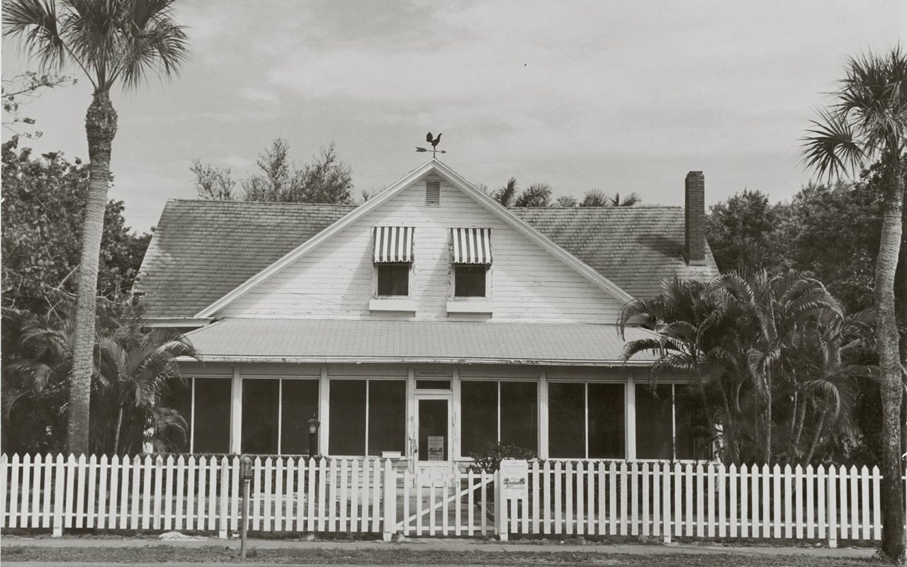 Historic Palm Cottage in Naples, with its screened porch, palm trees, and white picket fence.