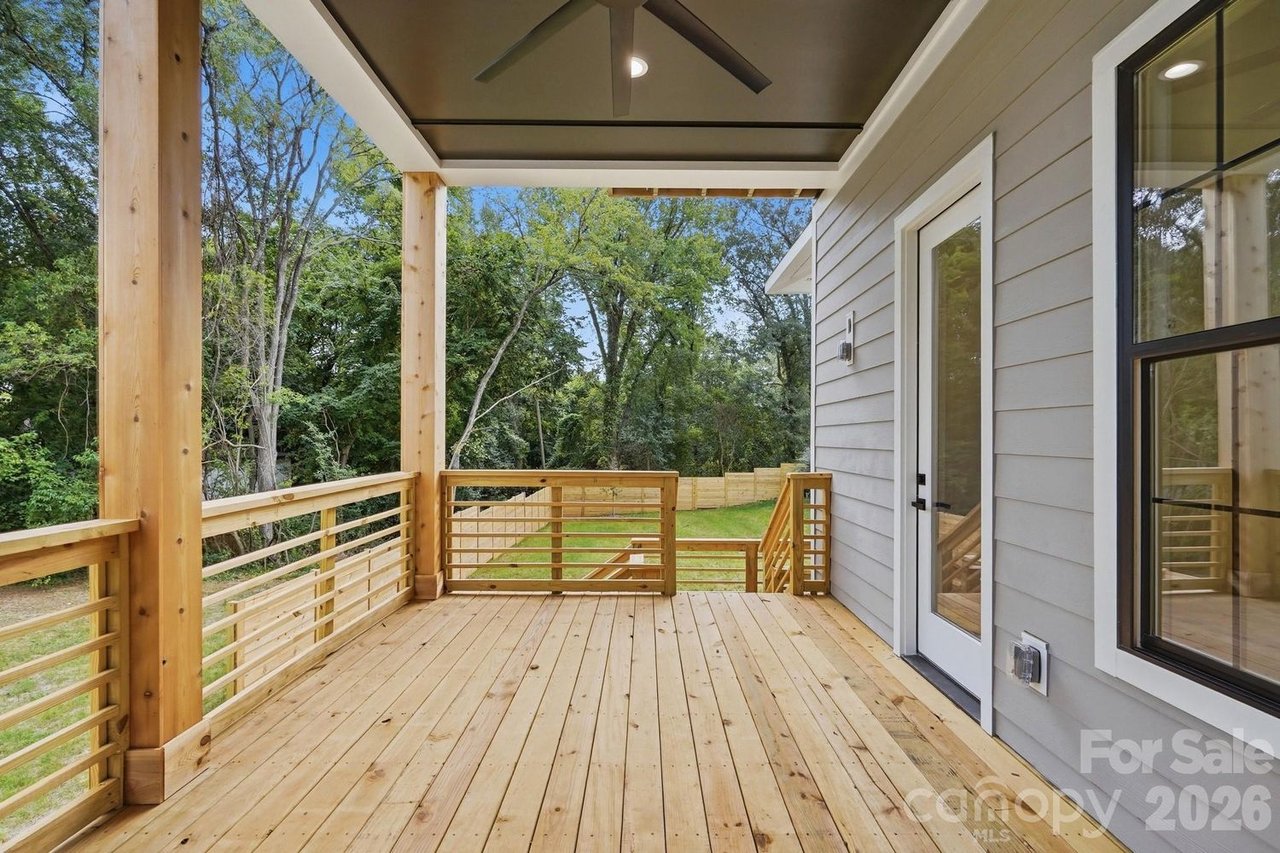Covered wooden back porch with gray siding, black-framed windows, and a wooded backyard.