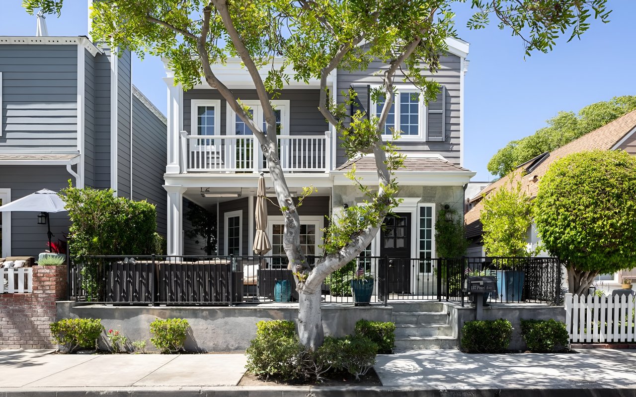  A beautiful two-story gray house with a small balcony and a front patio, with a green tree in front.