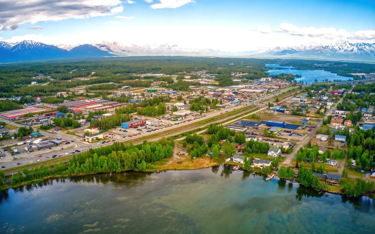 Wasilla’s riverfront and commercial district, with a lake and snow-capped mountains beyond.