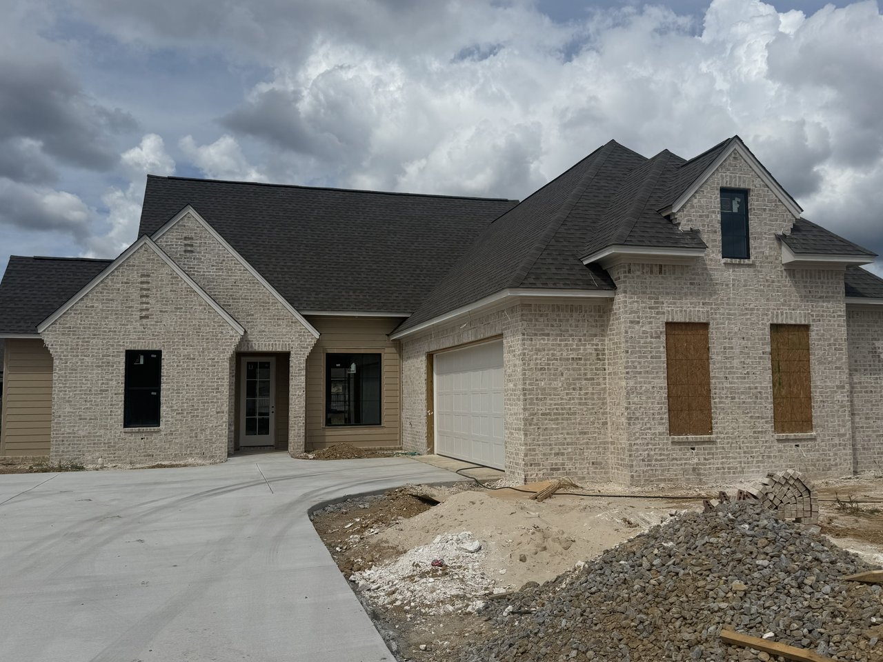 Newly built brick home with plywood-covered windows and construction debris in the foreground.