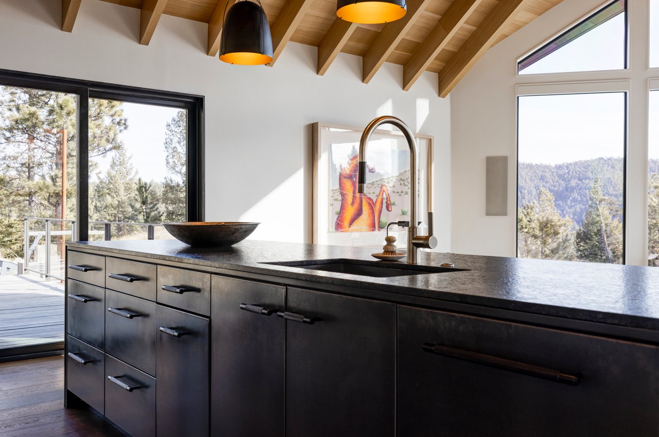 High-end Boulder kitchen counter with black cabinetry, brass faucet, and panoramic mountain views through windows