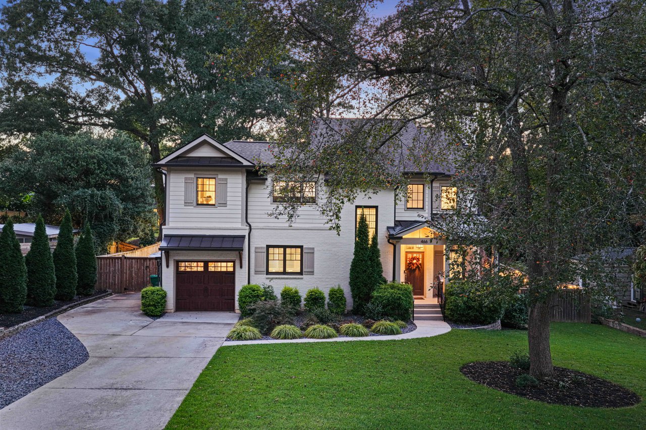 Two-story white home at dusk, framed by mature trees, with a lit entry and attached garage.