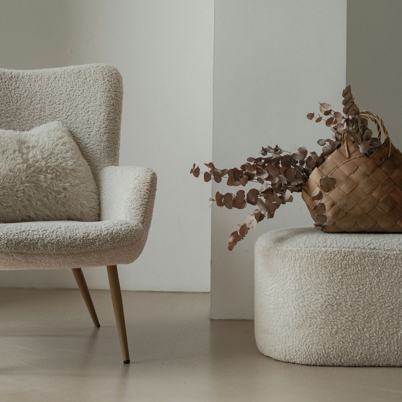 Cream bouclé chair and upholstered stool with a woven basket of dried foliage.
