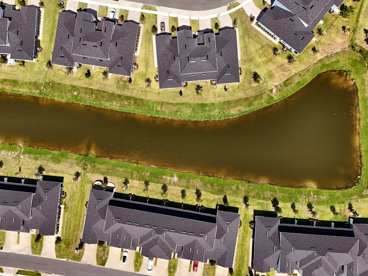 Aerial view of homes bordering a long pond, with lawns and neighboring houses.