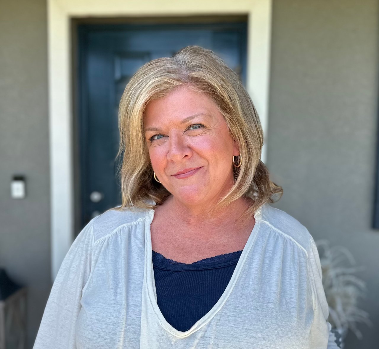 Cynthia Robinson in a pale cardigan, standing in front of a dark blue doorway.