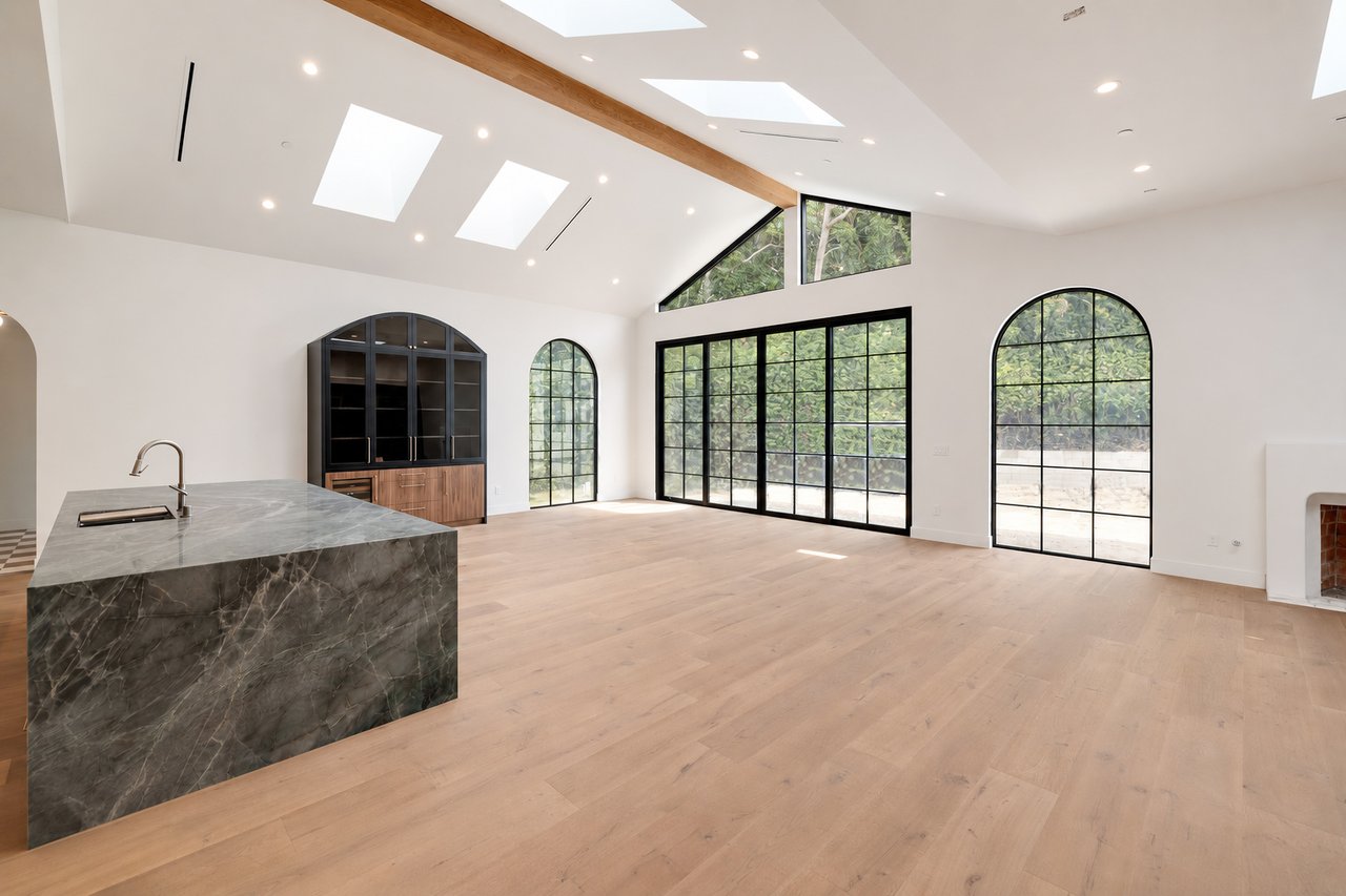 Open-plan kitchen with a dark marble island, vaulted skylit ceiling, and black-framed arched windows.