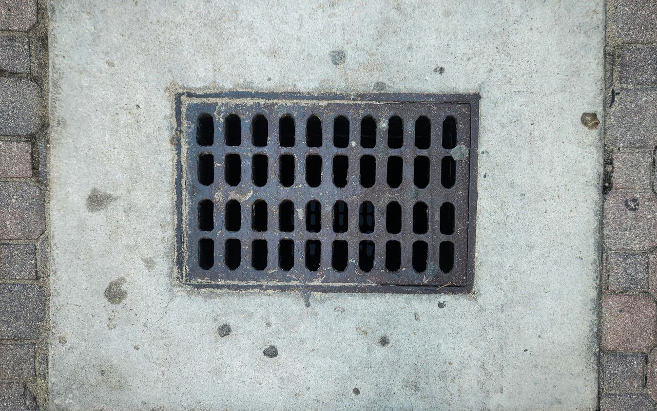 Metal storm drain grate set into a concrete sidewalk.