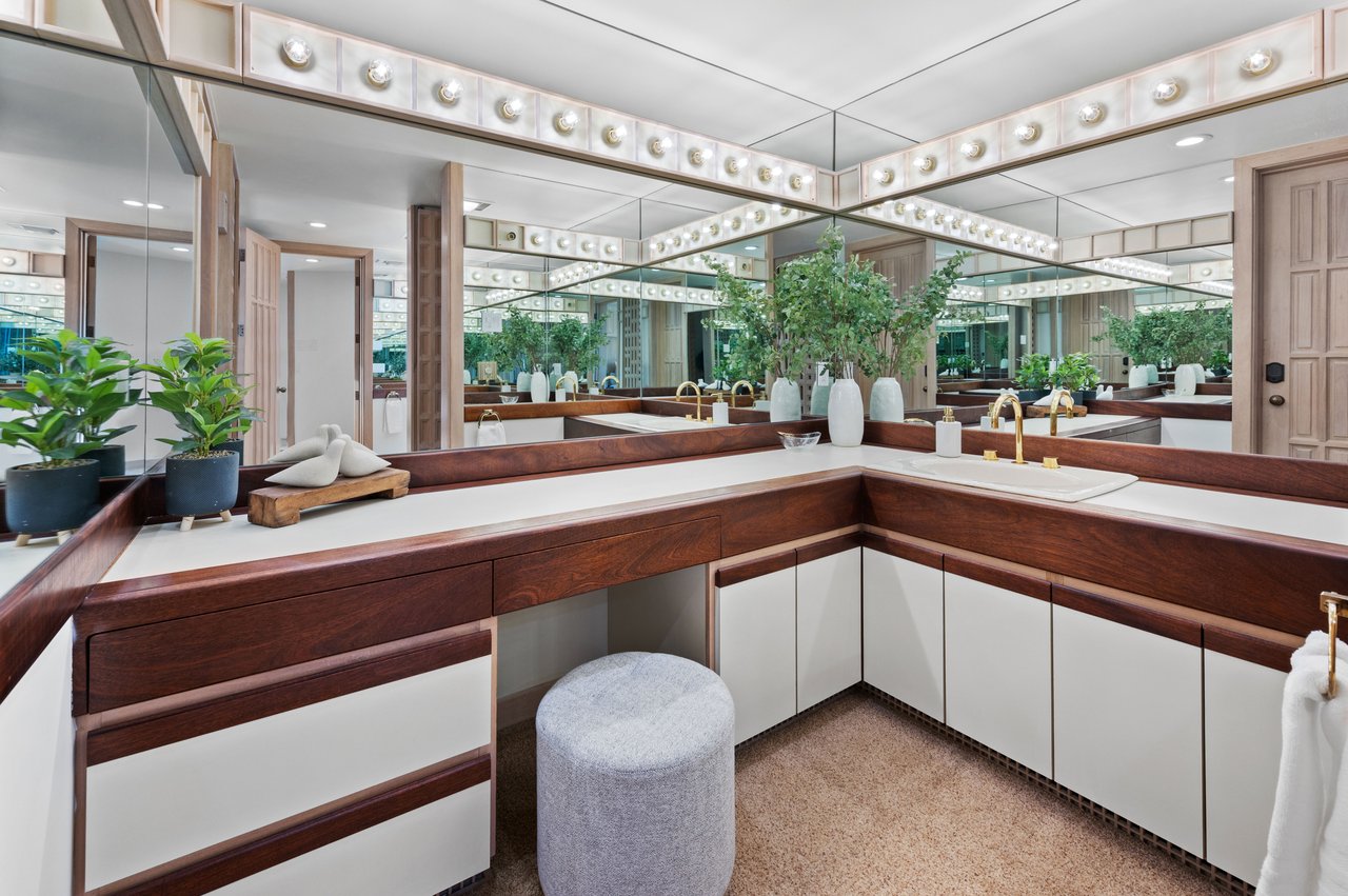 Bathroom with a long dark wood vanity, expansive mirrors, and rows of vanity lights.