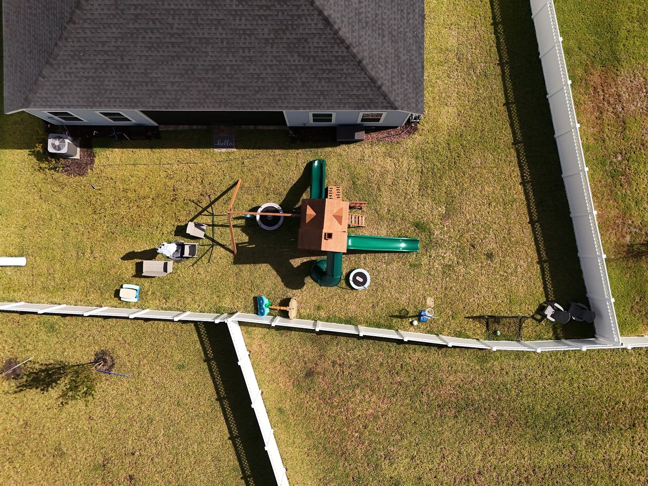 Fenced backyard with a wooden playset and green slides, viewed from above.