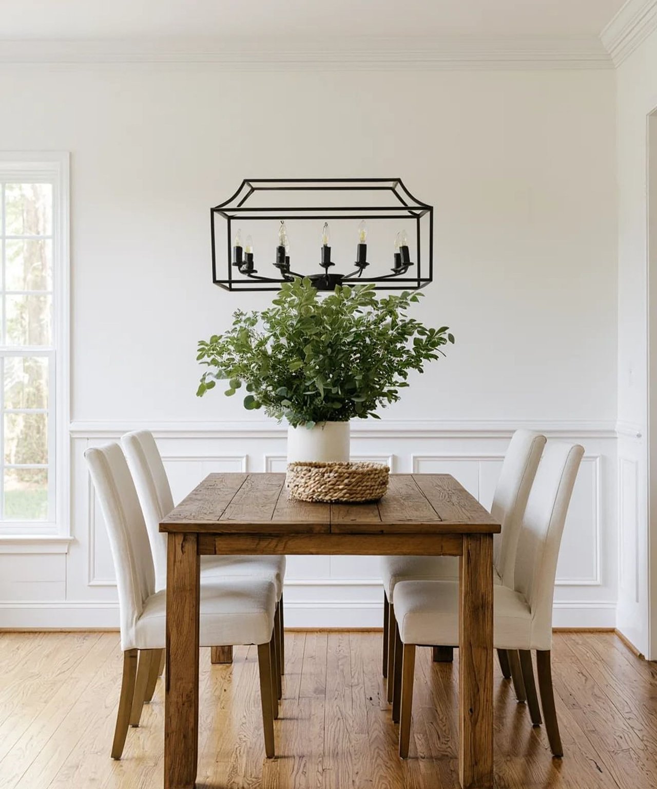 Dining room with a rustic wood table, cream chairs, and a black geometric chandelier.