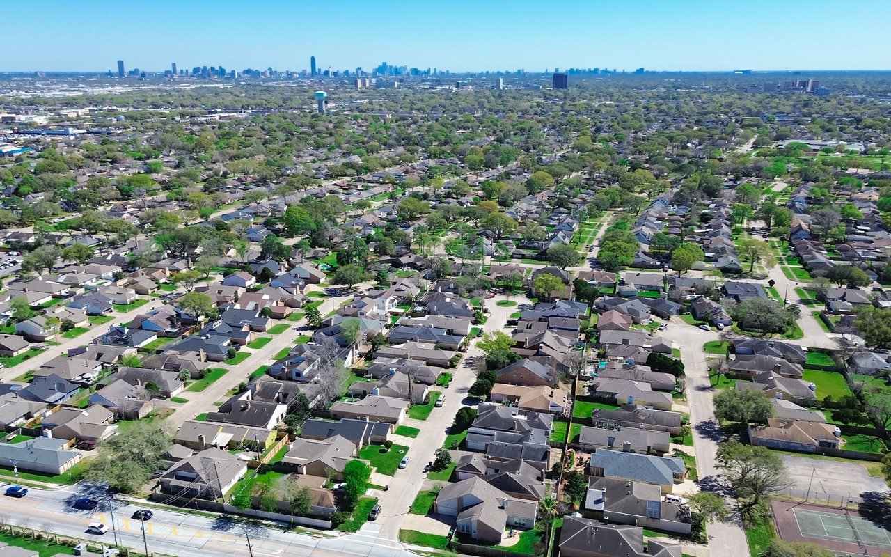Aerial view of a tree-lined suburban neighborhood with a distant city skyline.
