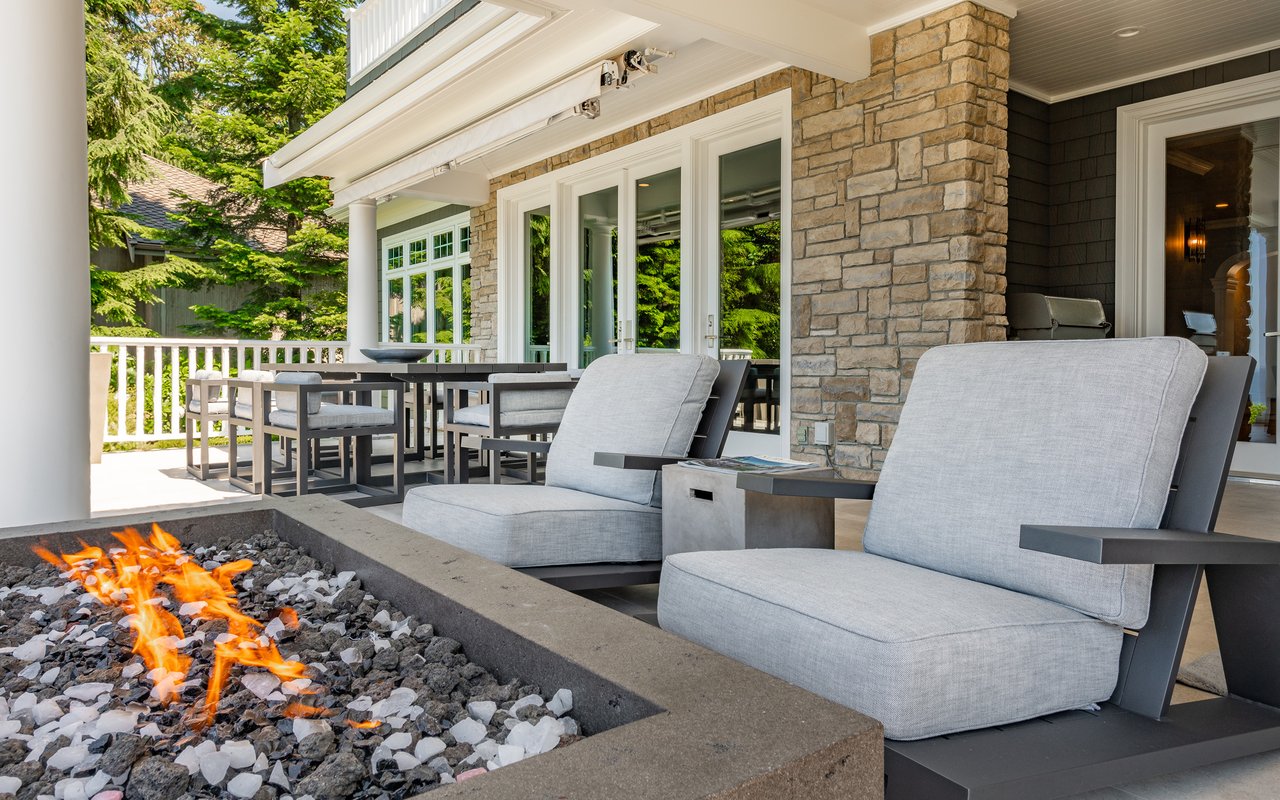 Covered patio with a stone fire pit, gray lounge chairs, and an outdoor dining area.