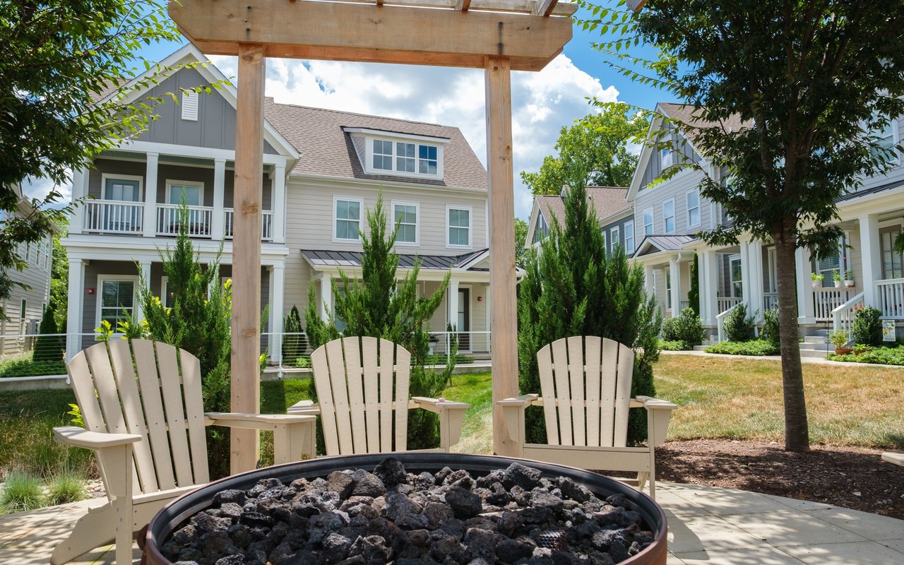 Residential courtyard with a pergola, three Adirondack chairs, and a stone-filled fire pit.