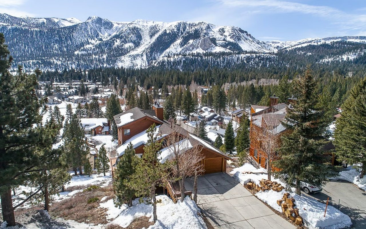Snow-covered homes and pine trees beneath a wide mountain range.