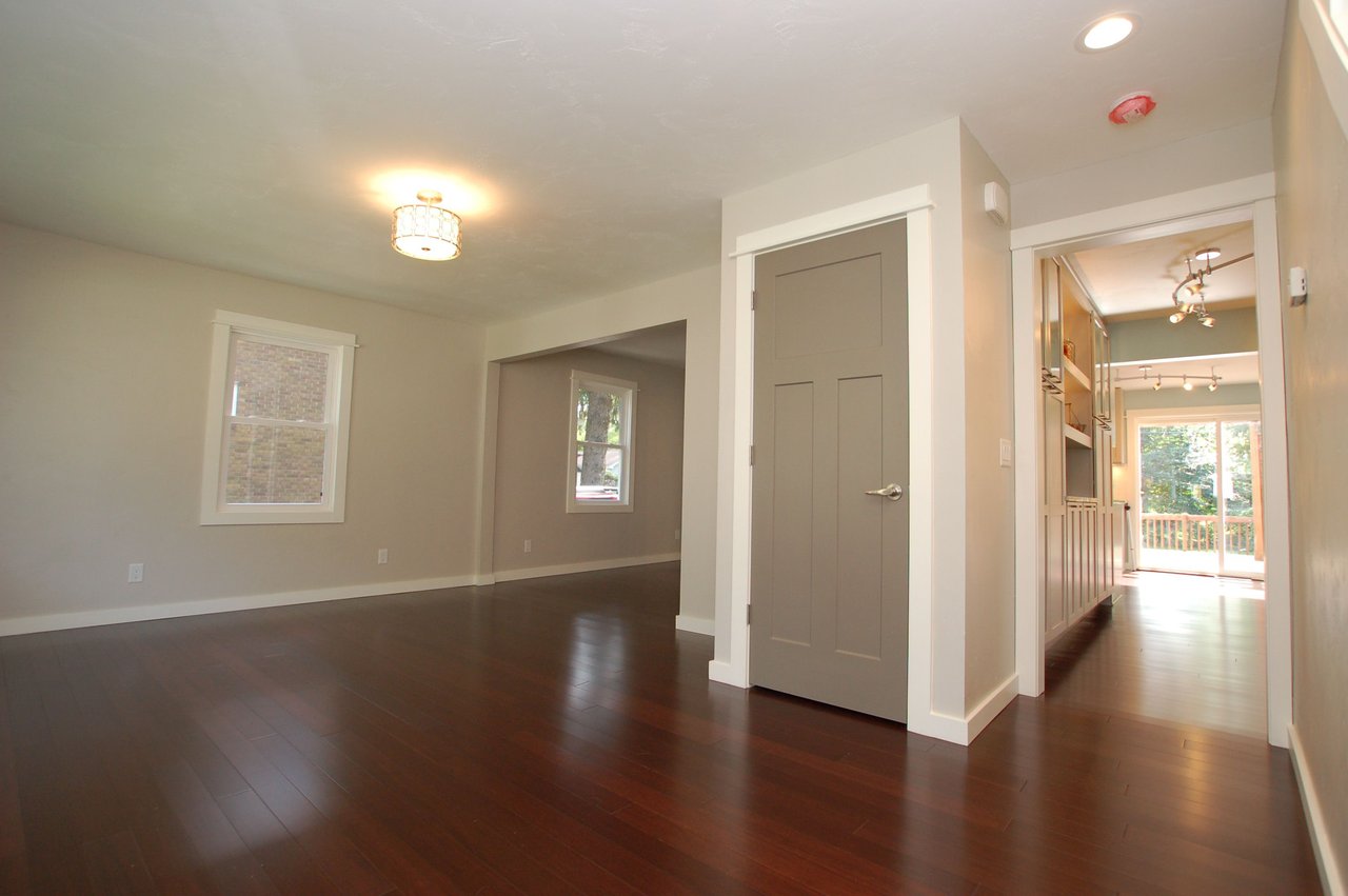 Empty interior with dark hardwood floors, a paneled door, and a view into the kitchen.