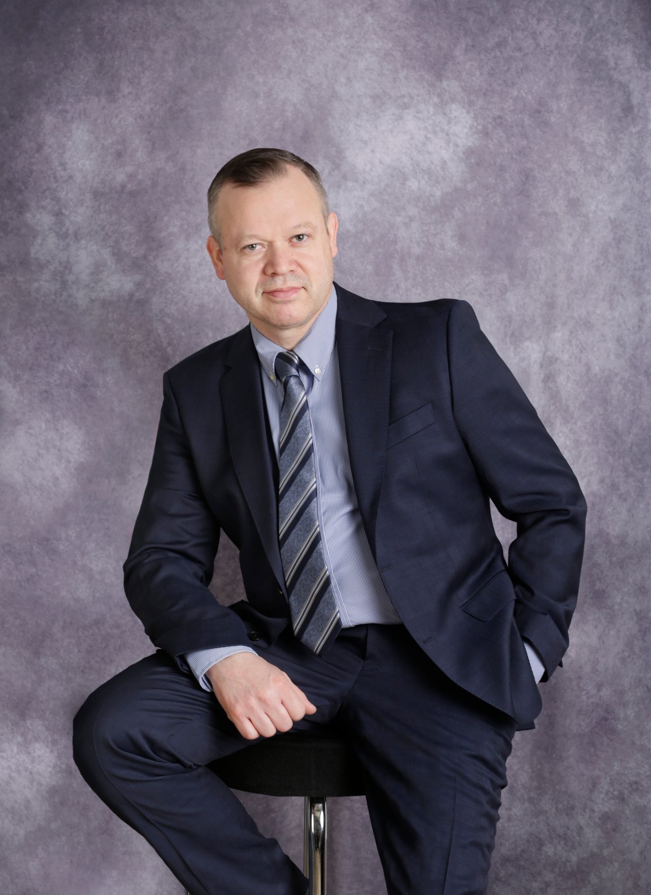 Fernando Aguilar seated in a navy suit against a mottled gray-purple backdrop.