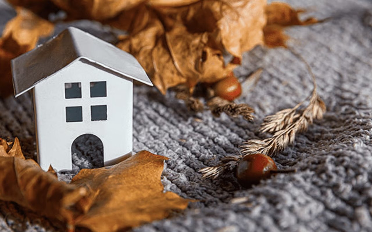 White model house among dry autumn leaves on gray knitted fabric.