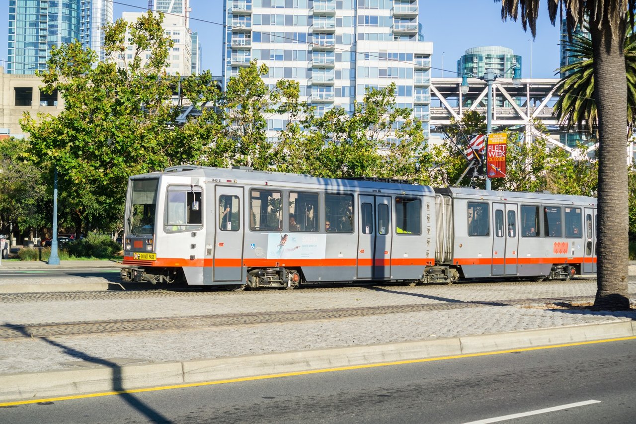 A T Third Muni light-rail train approaching downtown San Francisco at sunset, with the city skyline in the background.