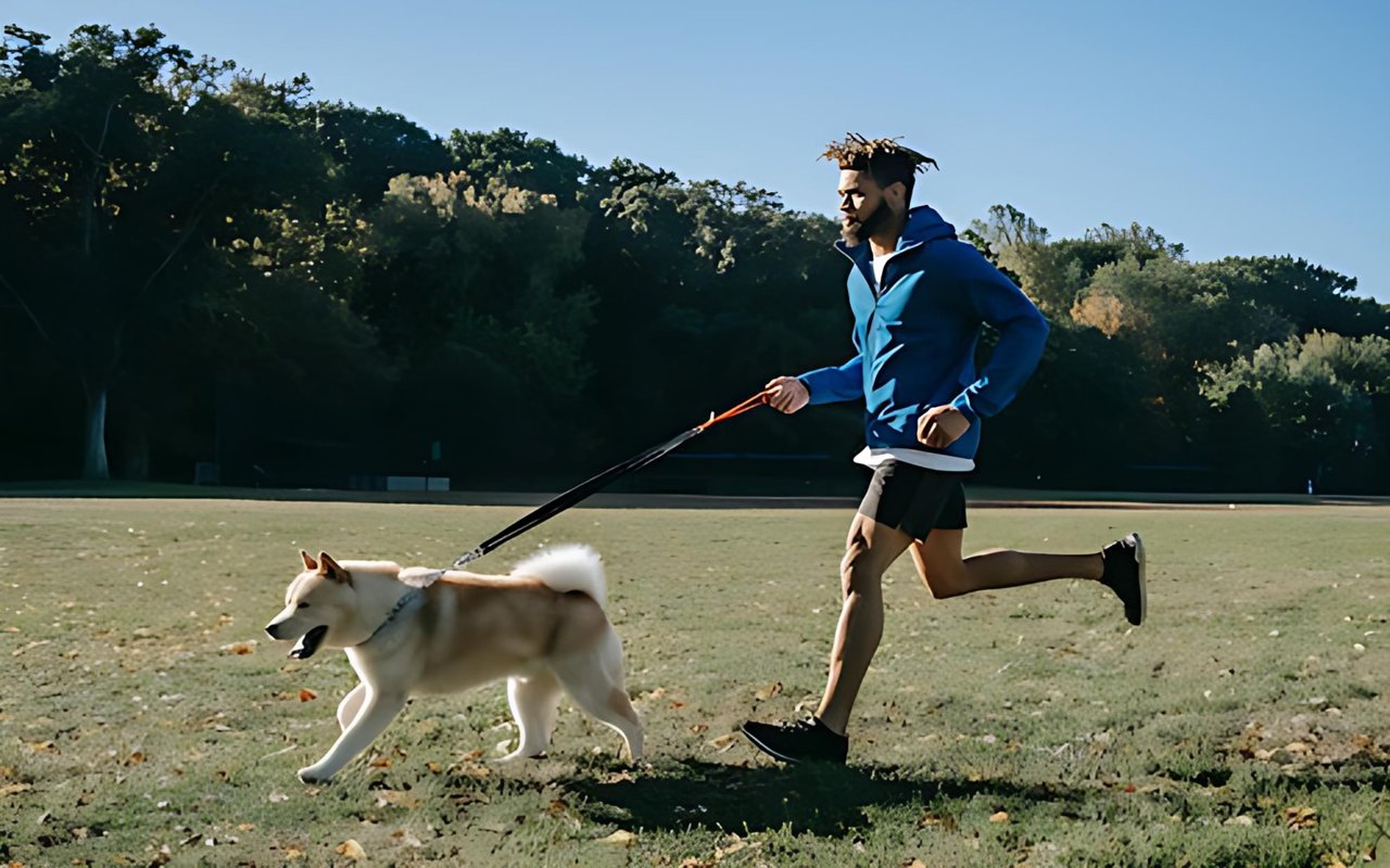 A man jogs with a leashed dog across a grassy park.