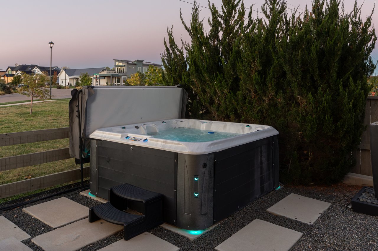 Hot tub with lit interior beside tall evergreens at dusk