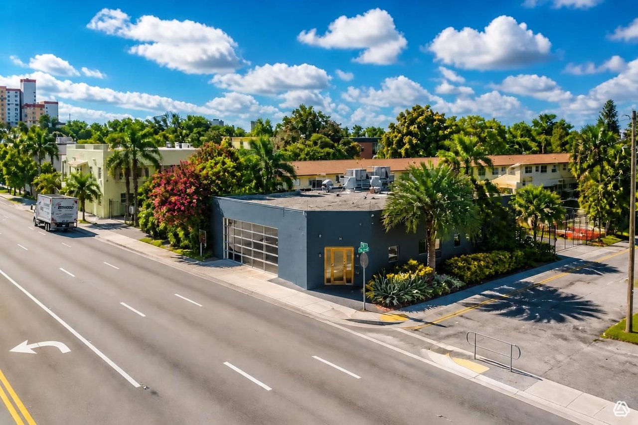 Street-corner property with a dark blue-gray facade, gold-framed entrance, and tropical landscaping.