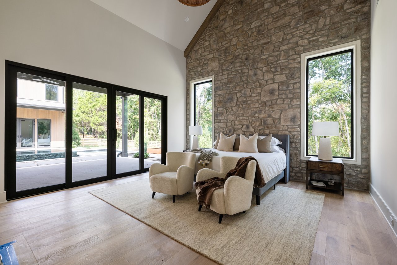 Bedroom with a tall stone accent wall, vaulted ceiling, and glass doors opening to a patio and pool.
