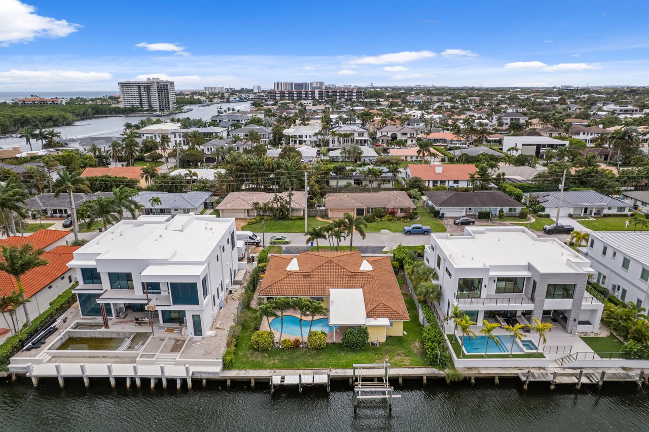 Aerial view of waterfront homes and docks, with swimming pools and a canal in the foreground.