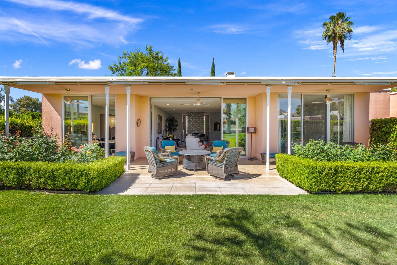 Rear patio of a single-story home with outdoor seating, sliding glass doors, clipped hedges, and lawn.