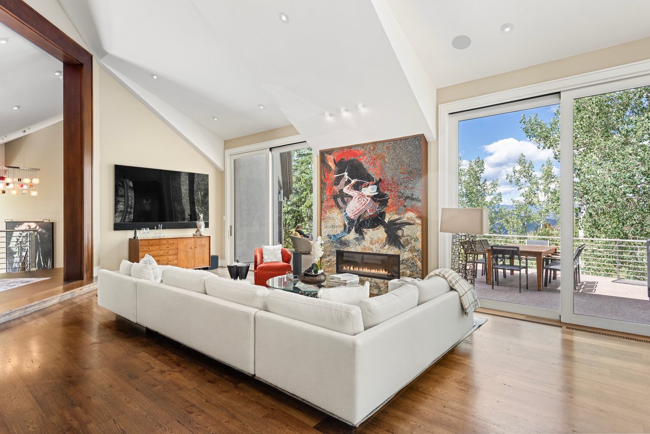 Living room with vaulted ceiling, white sectional, fireplace, and sliding doors to a tree-lined patio.