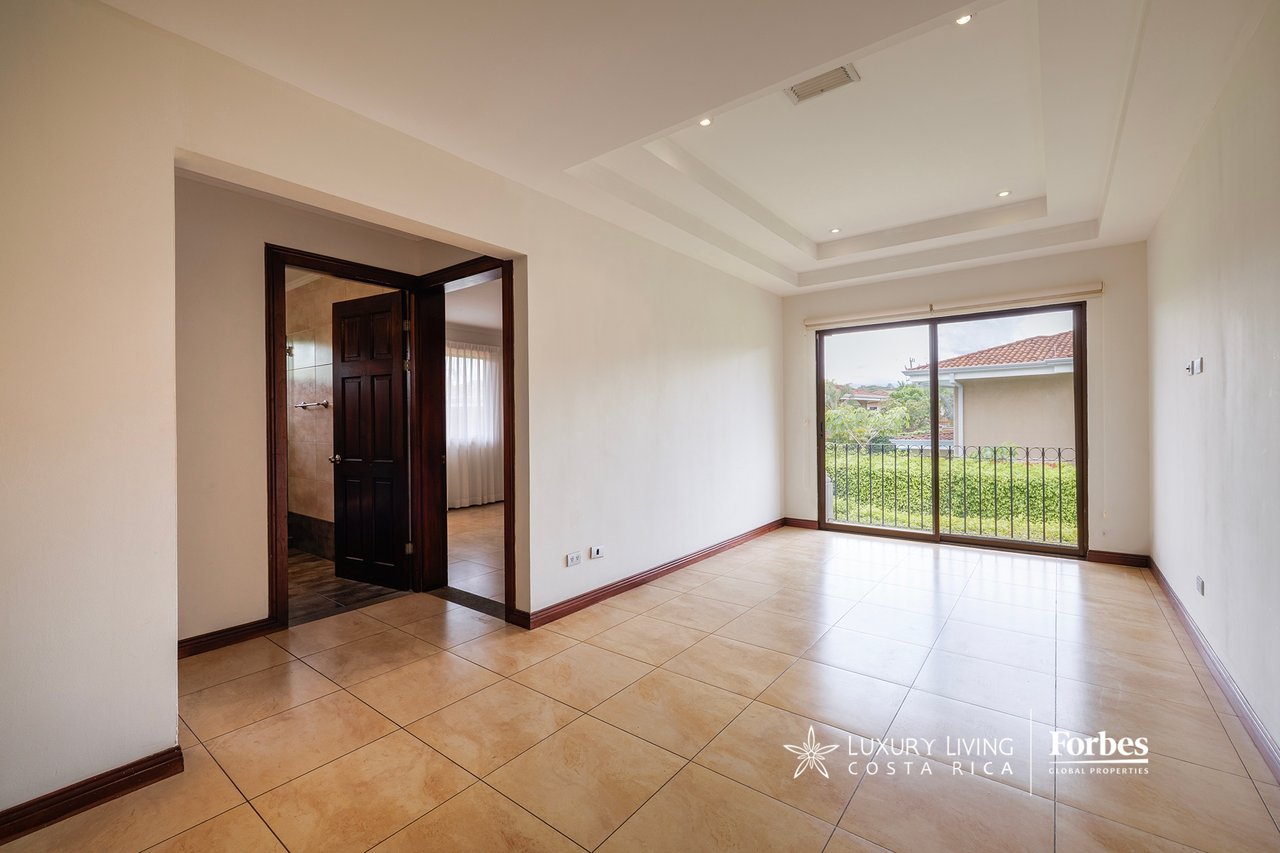 Empty tiled bedroom with sliding glass doors opening onto a terrace overlooking greenery.