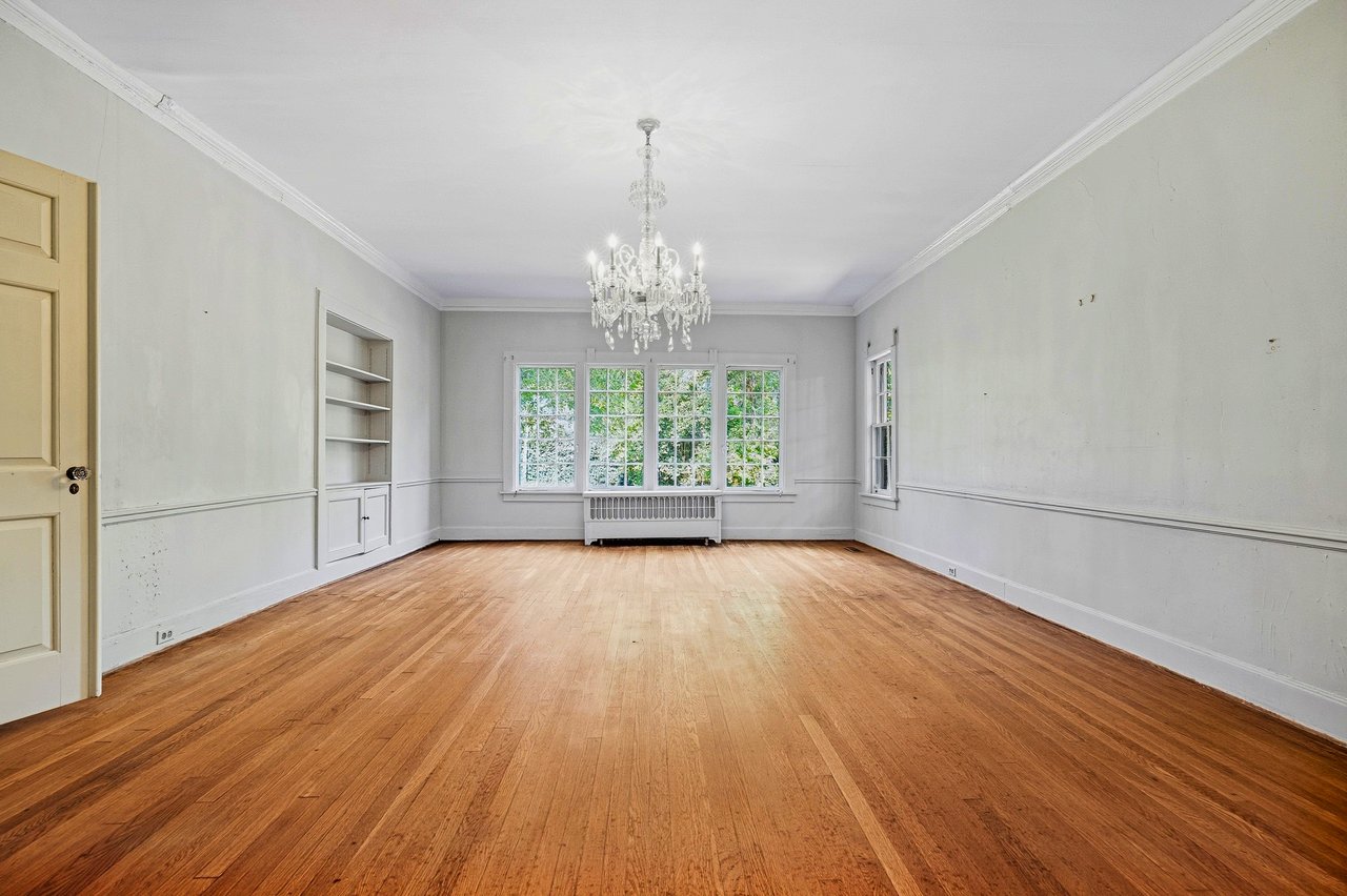 Empty room with hardwood floors, built-in shelving, large windows, and a crystal chandelier.