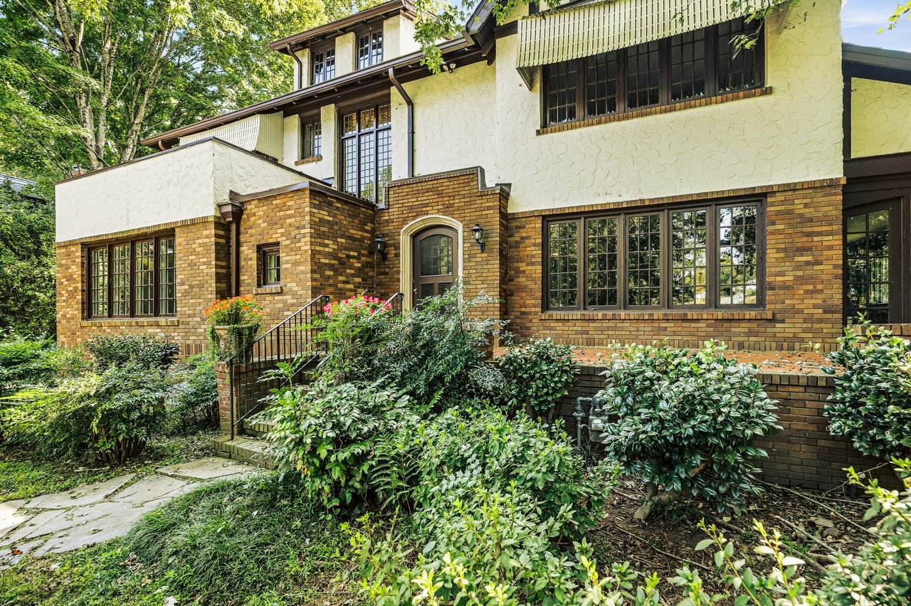 Multi-story brick and stucco house with an arched entry and leafy garden.