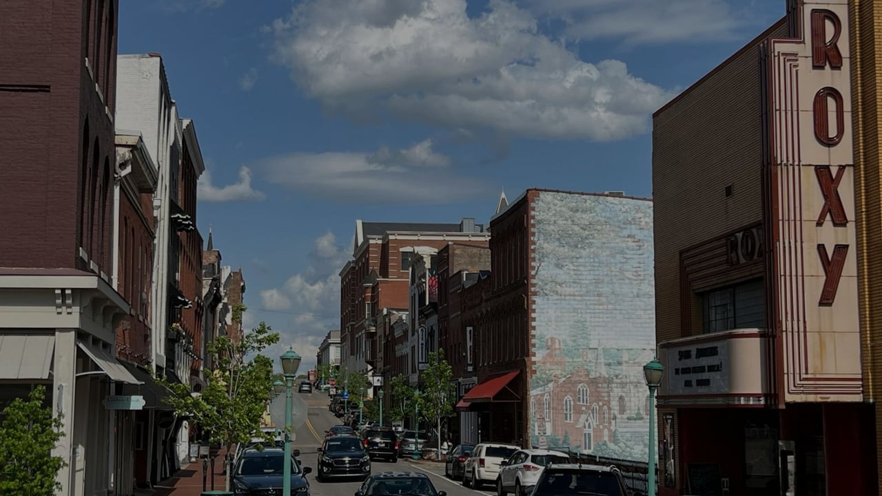 Downtown street with historic storefronts, a painted mural, and a theater marked ROXY.