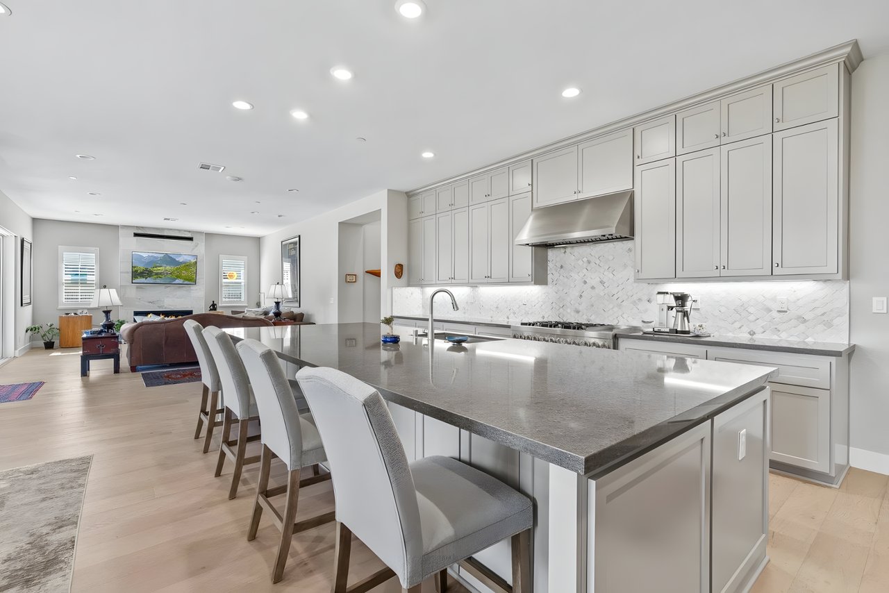 Bright kitchen with a large gray island and white cabinetry opening to a furnished living room.