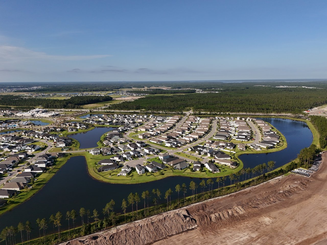 Aerial view of a residential neighborhood with curving streets, ponds, and forest beyond.