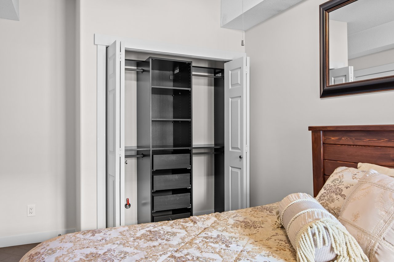 Bedroom with an open closet organizer and a patterned bed with pillows.