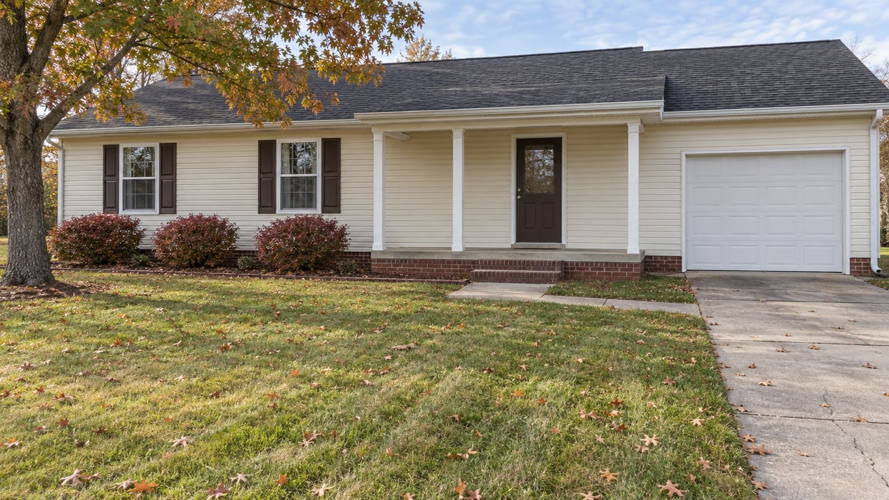 Cream-sided single-story home with a brick-based front porch, broad autumn lawn and mature oak.