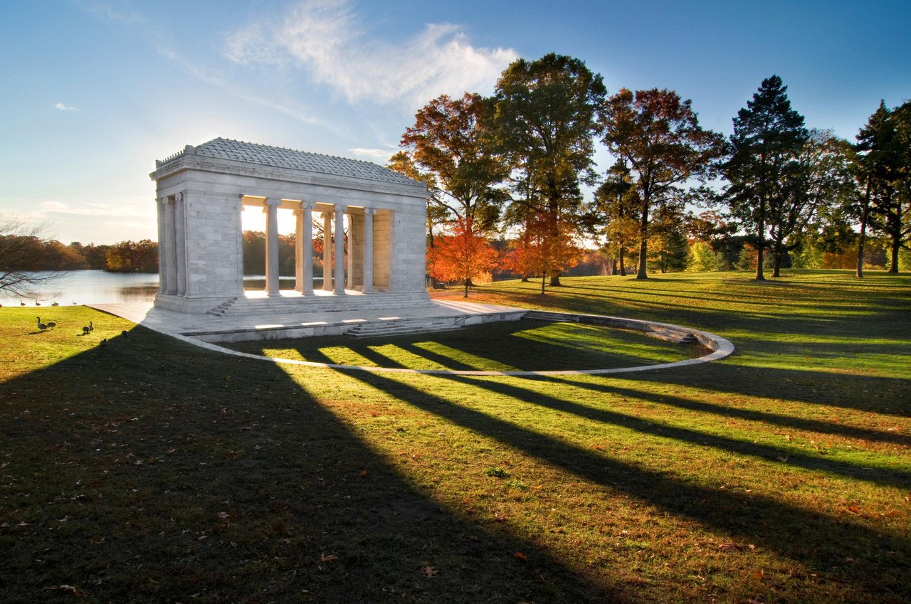 Marble Temple to Music pavilion beside a pond, framed by autumn foliage and long evening shadows.