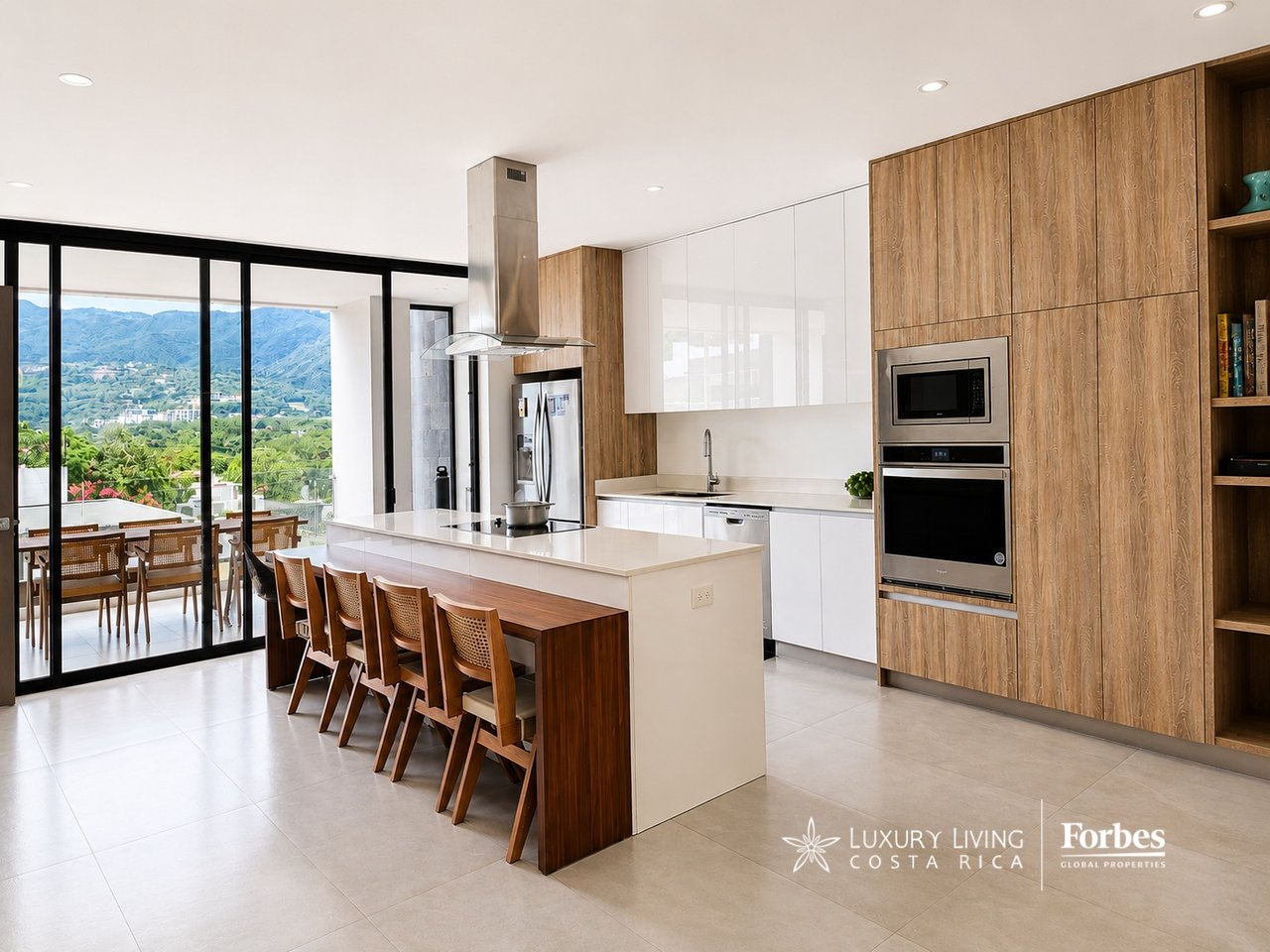 Contemporary kitchen with a white island, wood cabinetry, and mountain views through glass doors.